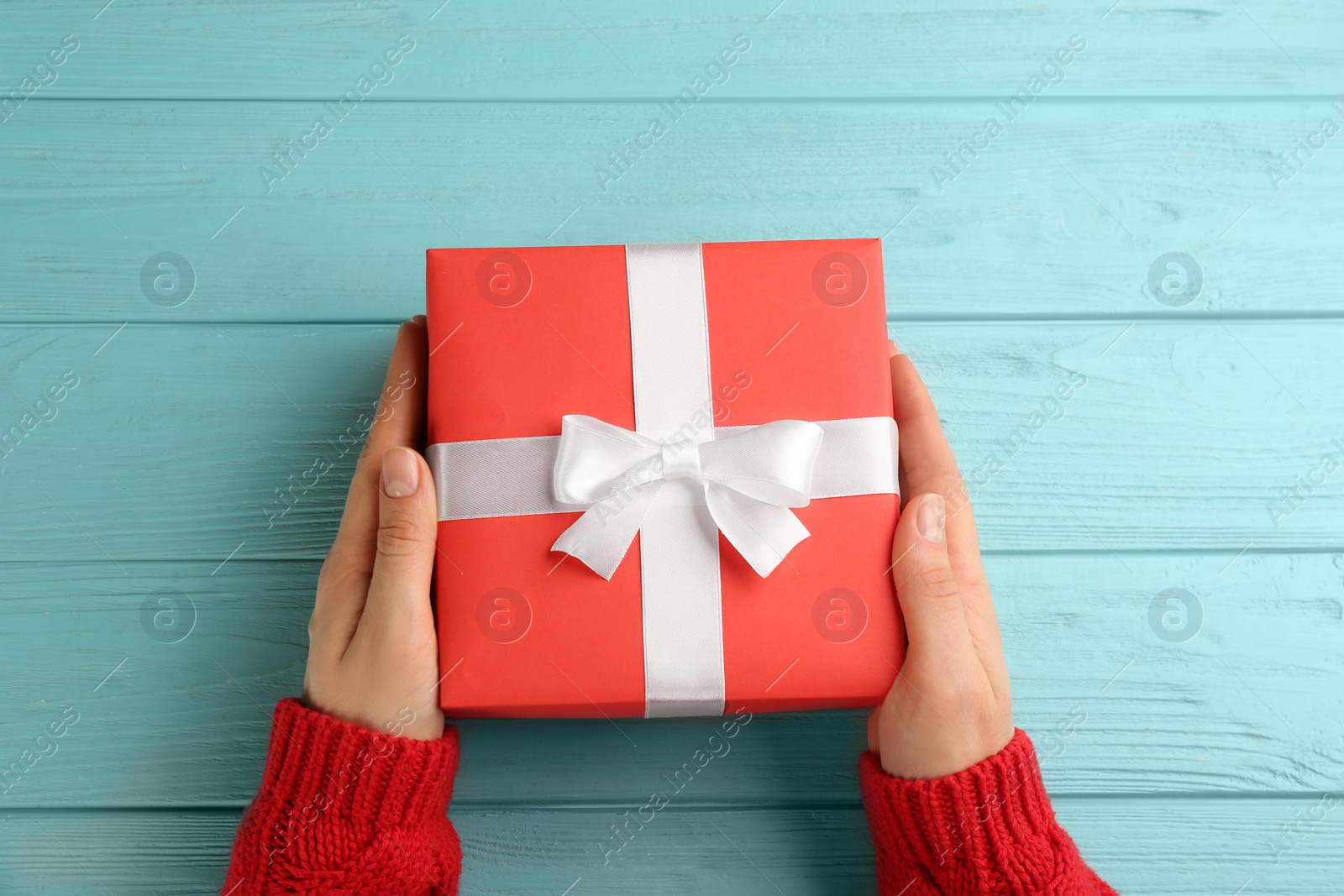 Photo of Woman holding gift box at turquoise wooden table, top view. Valentine's Day celebration