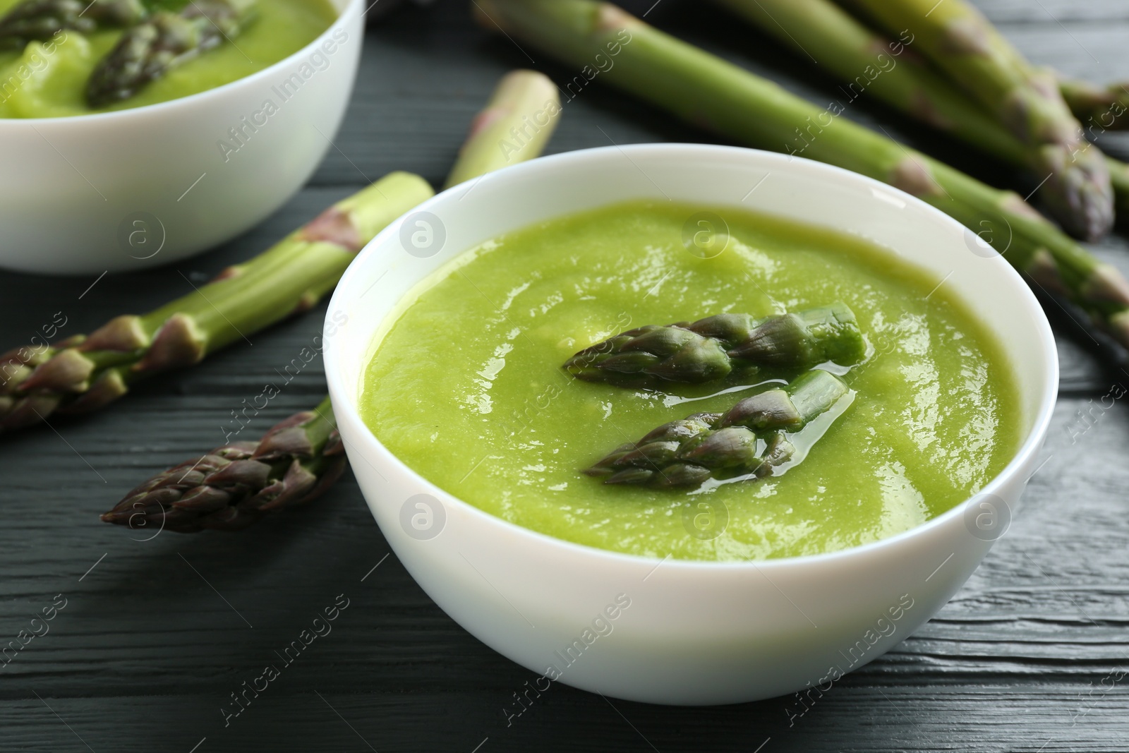 Photo of Delicious asparagus soup in bowl on grey wooden table