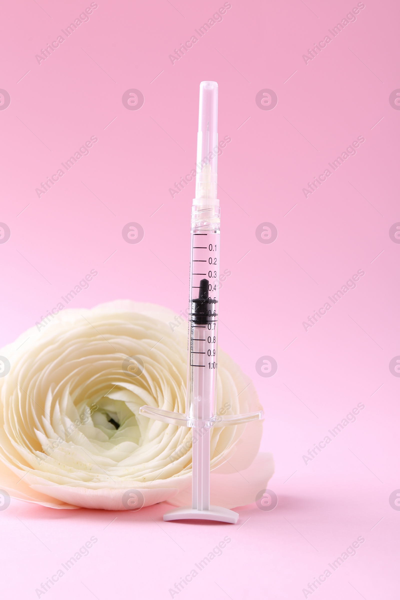 Photo of Cosmetology. Medical syringe and ranunculus flower on pink background