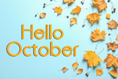 Text Hello October and golden autumn leaves on light blue background, top view