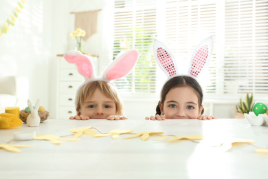 Cute children wearing bunny ears headbands at table with Easter eggs, indoors