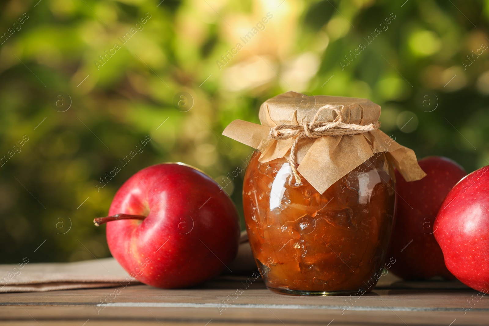 Photo of Glass jar with delicious apple jam and fresh fruits on wooden table against blurred background, closeup. Space for text