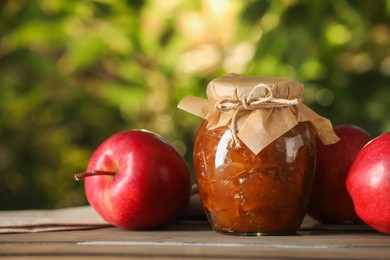 Photo of Glass jar with delicious apple jam and fresh fruits on wooden table against blurred background, closeup. Space for text