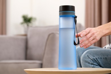 Woman taking bottle of water at wooden table indoors, closeup. Space for text