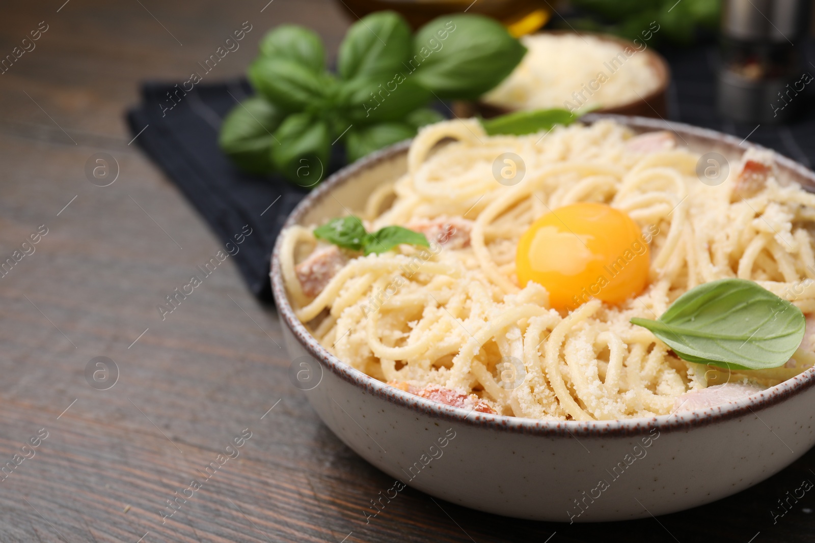 Photo of Bowl of tasty pasta Carbonara with basil leaves and egg yolk on wooden table, closeup. Space for text