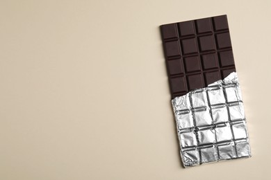 Photo of Delicious dark chocolate bar on beige background, top view. Space for text
