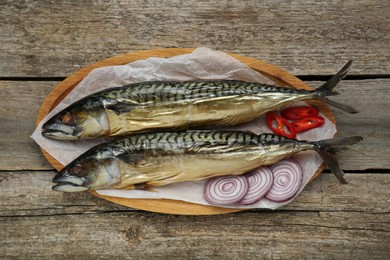 Photo of Delicious smoked mackerels, chili pepper and onion on wooden table, top view