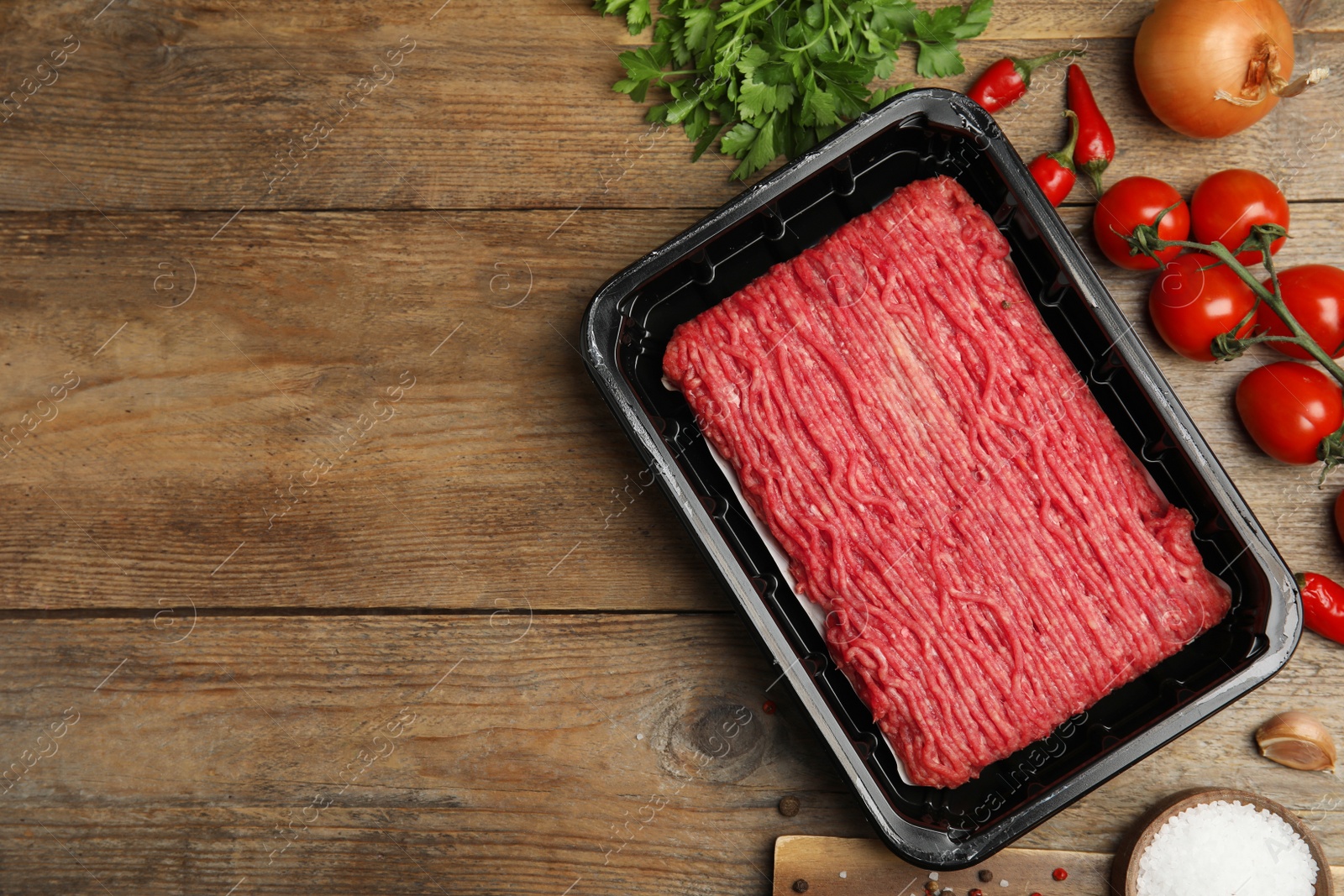 Photo of Raw fresh minced meat, tomatoes and other ingredients on wooden table, flat lay. Space for text