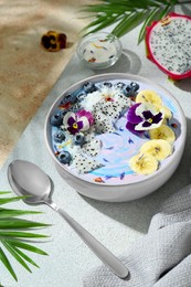 Delicious smoothie bowl with fresh fruits, blueberries and flowers served on color textured table