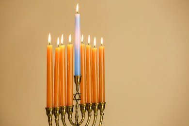Photo of Hanukkah celebration. Menorah with burning candles on beige background, space for text