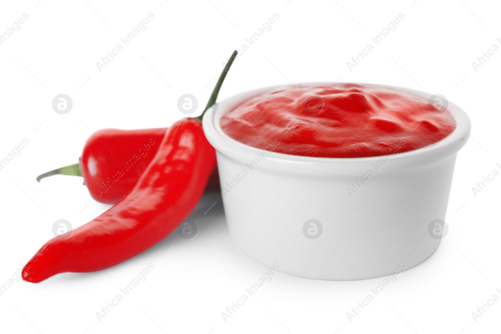 Photo of Bowl with red sauce and chili peppers isolated on white