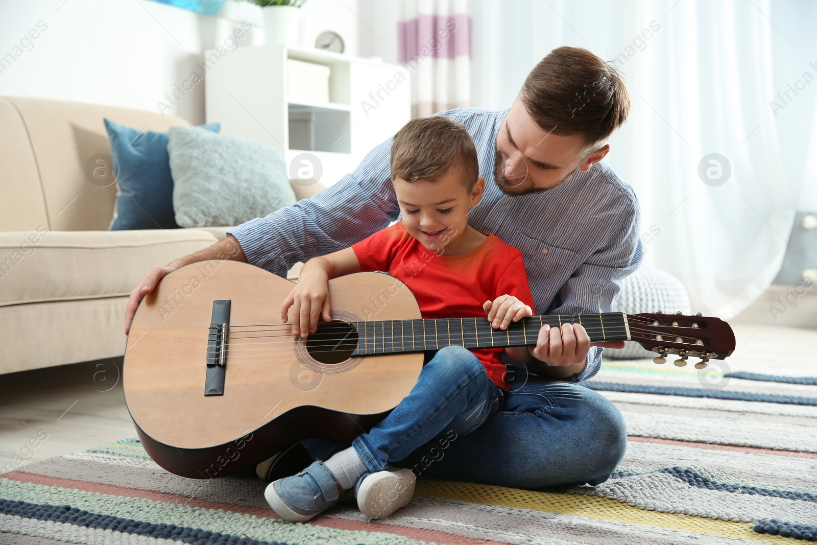 Photo of Father teaching his little son to play guitar at home