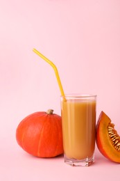 Tasty pumpkin juice in glass, whole and cut pumpkins on pale pink background