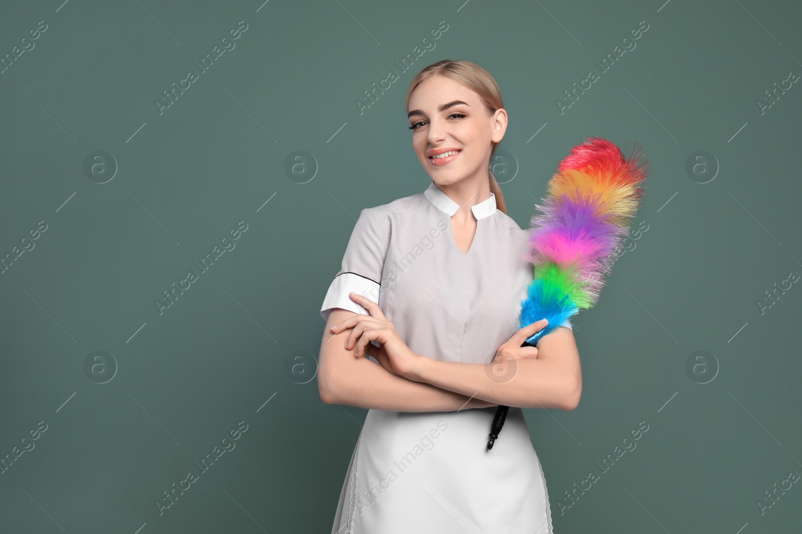 Photo of Young chambermaid with dusting brush on color background