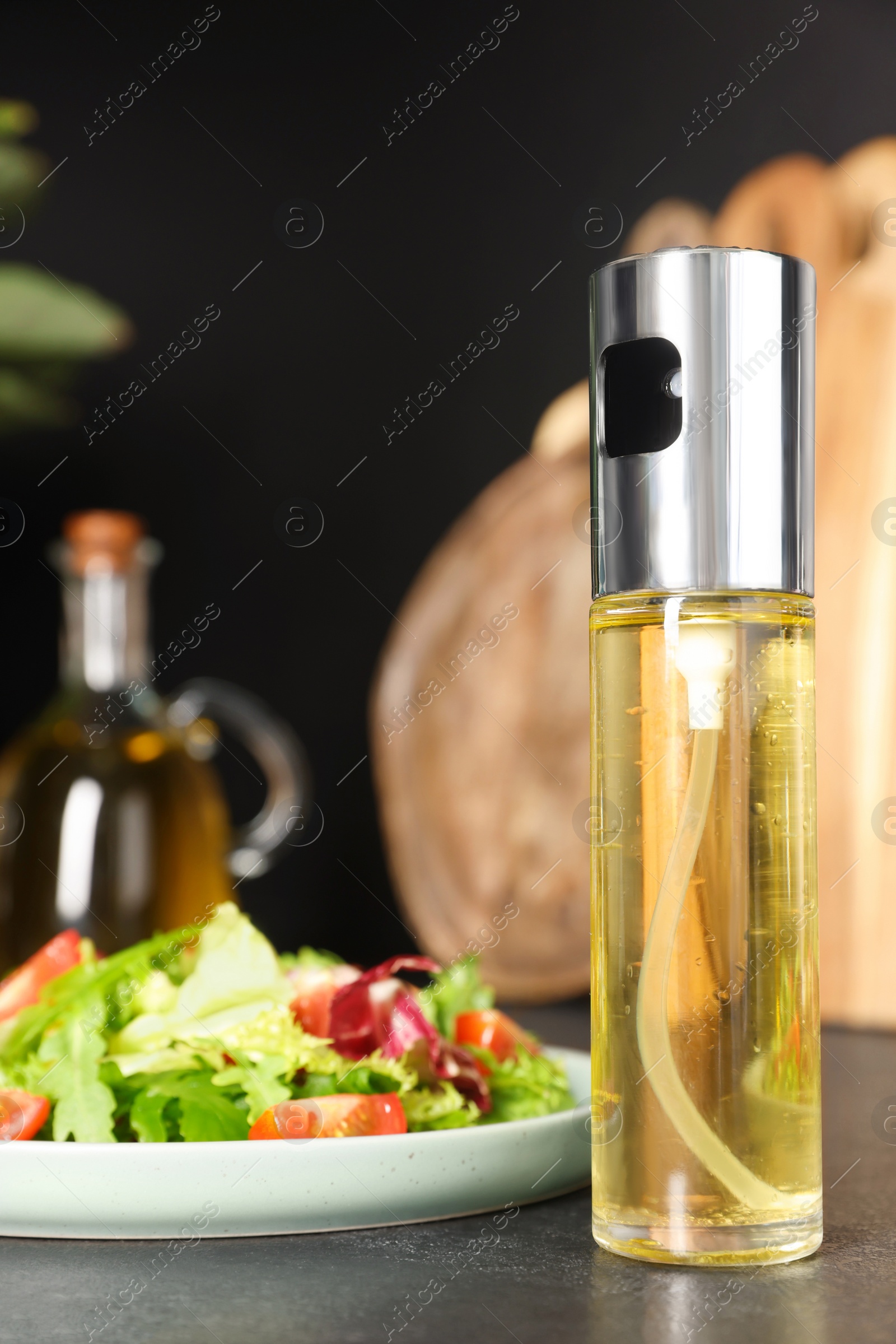 Photo of Plate of salad and spray bottle with cooking oil on black table in kitchen