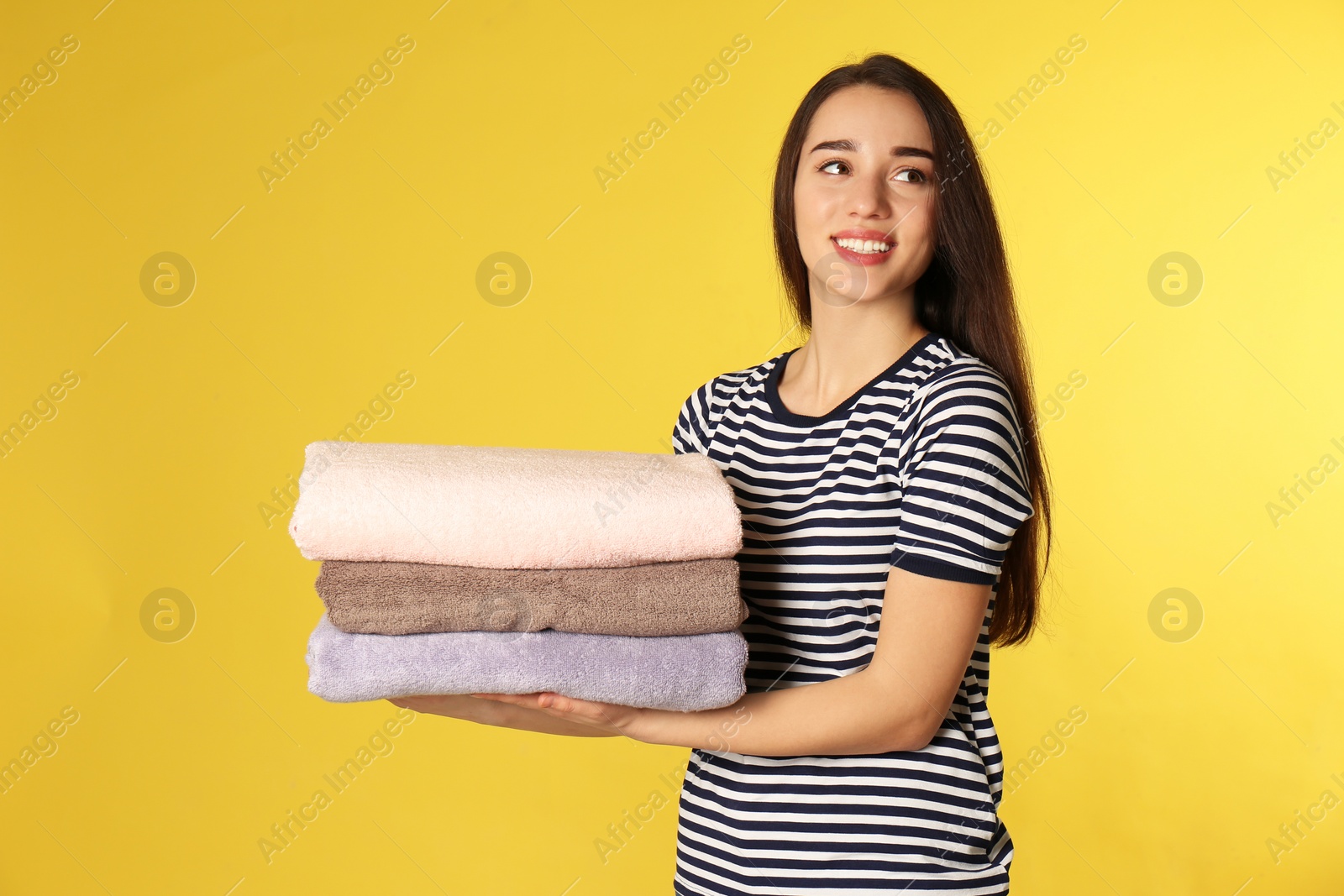 Photo of Happy young woman holding clean laundry on color background