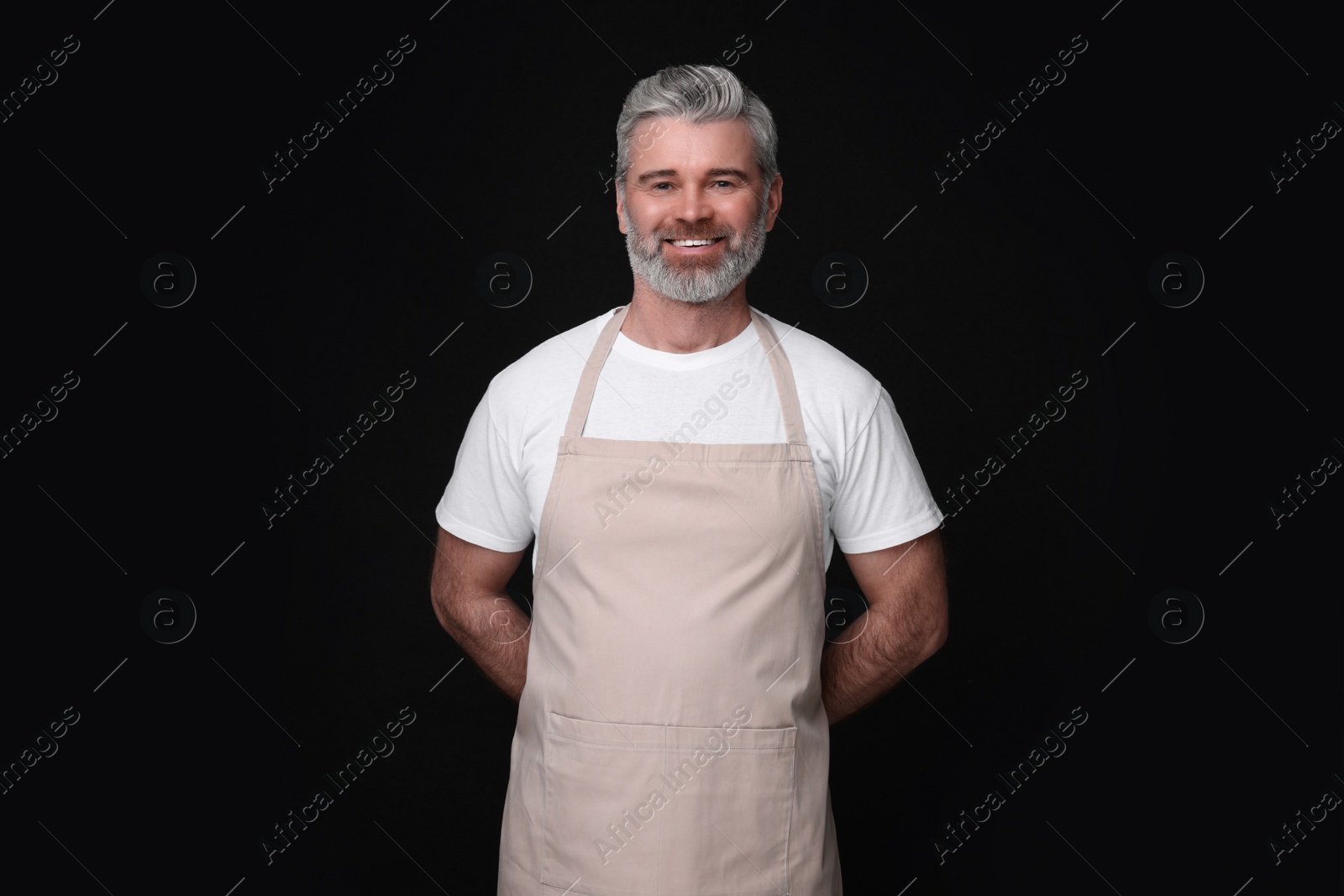 Photo of Happy man wearing kitchen apron on black background. Mockup for design