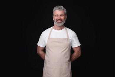 Photo of Happy man wearing kitchen apron on black background. Mockup for design