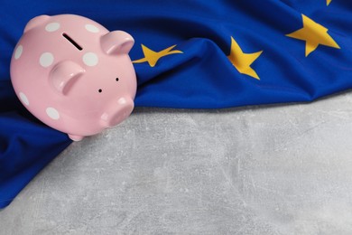 Photo of Pink piggy bank and flag of European Union on light grey table. Space for text