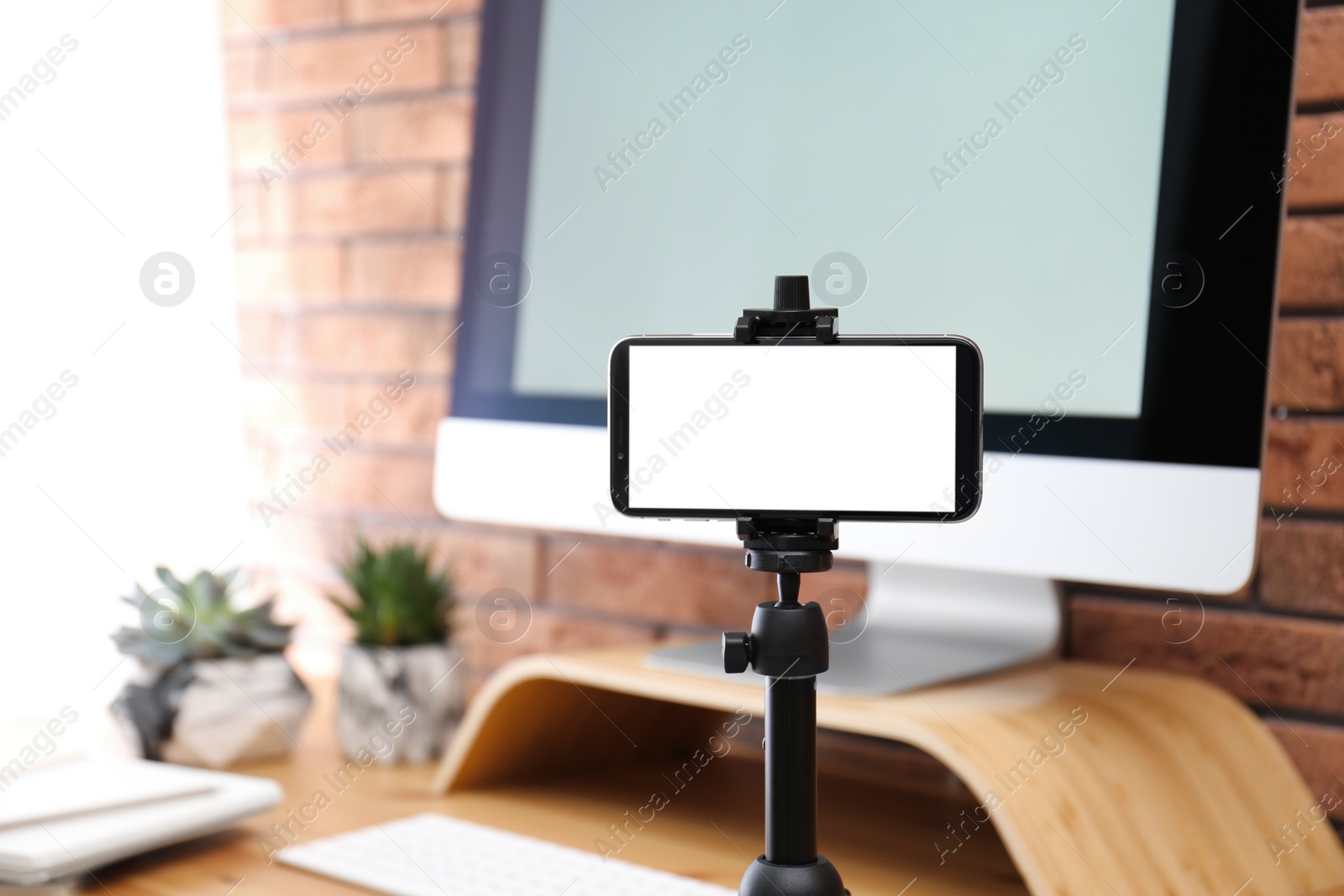 Photo of Stand with smartphone near computer on table indoors. Mockup for design