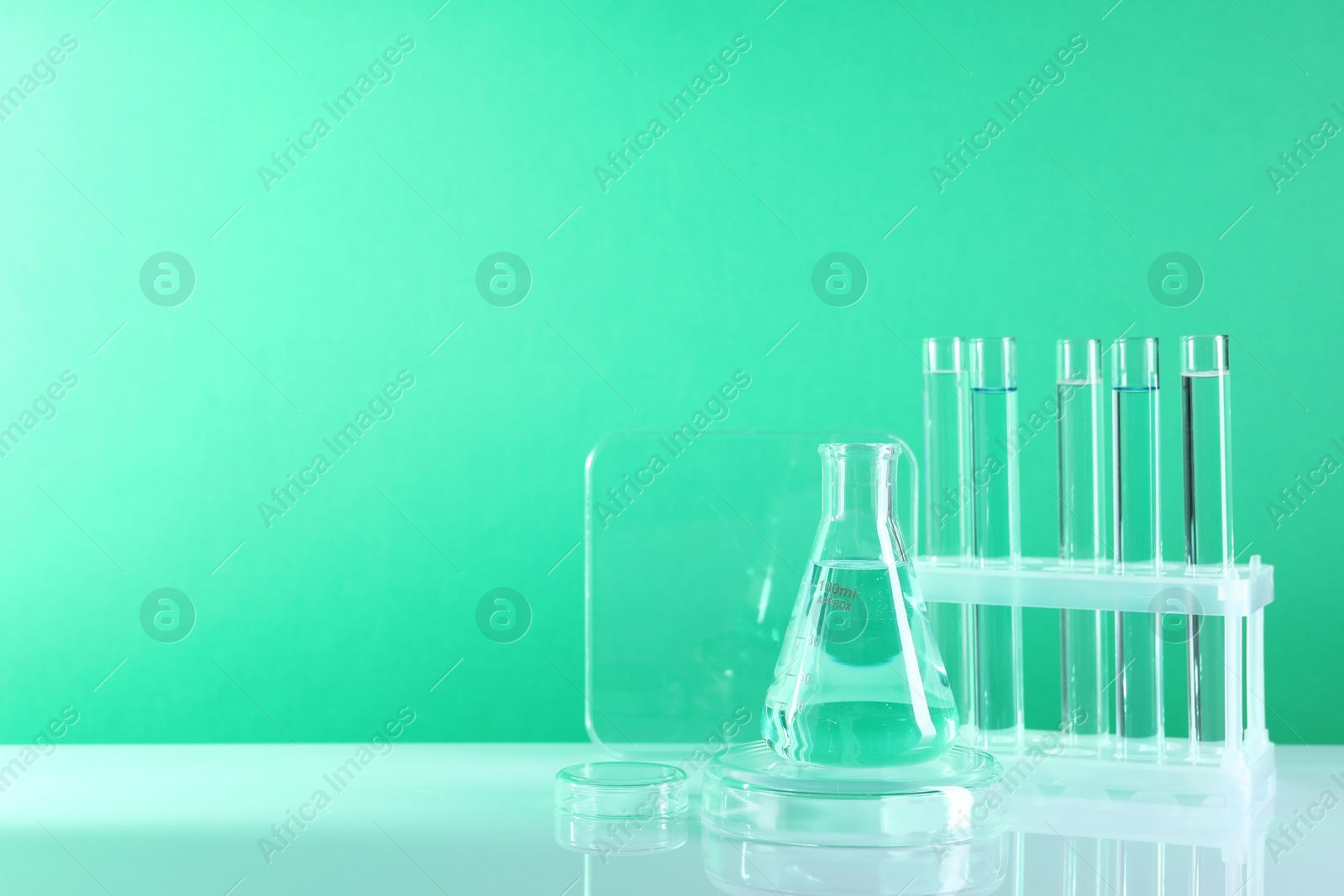 Photo of Laboratory analysis. Different glassware on table against green background, space for text