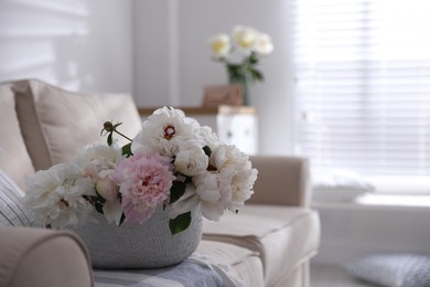 Bouquet of beautiful peony flowers in basket on sofa. Space for text