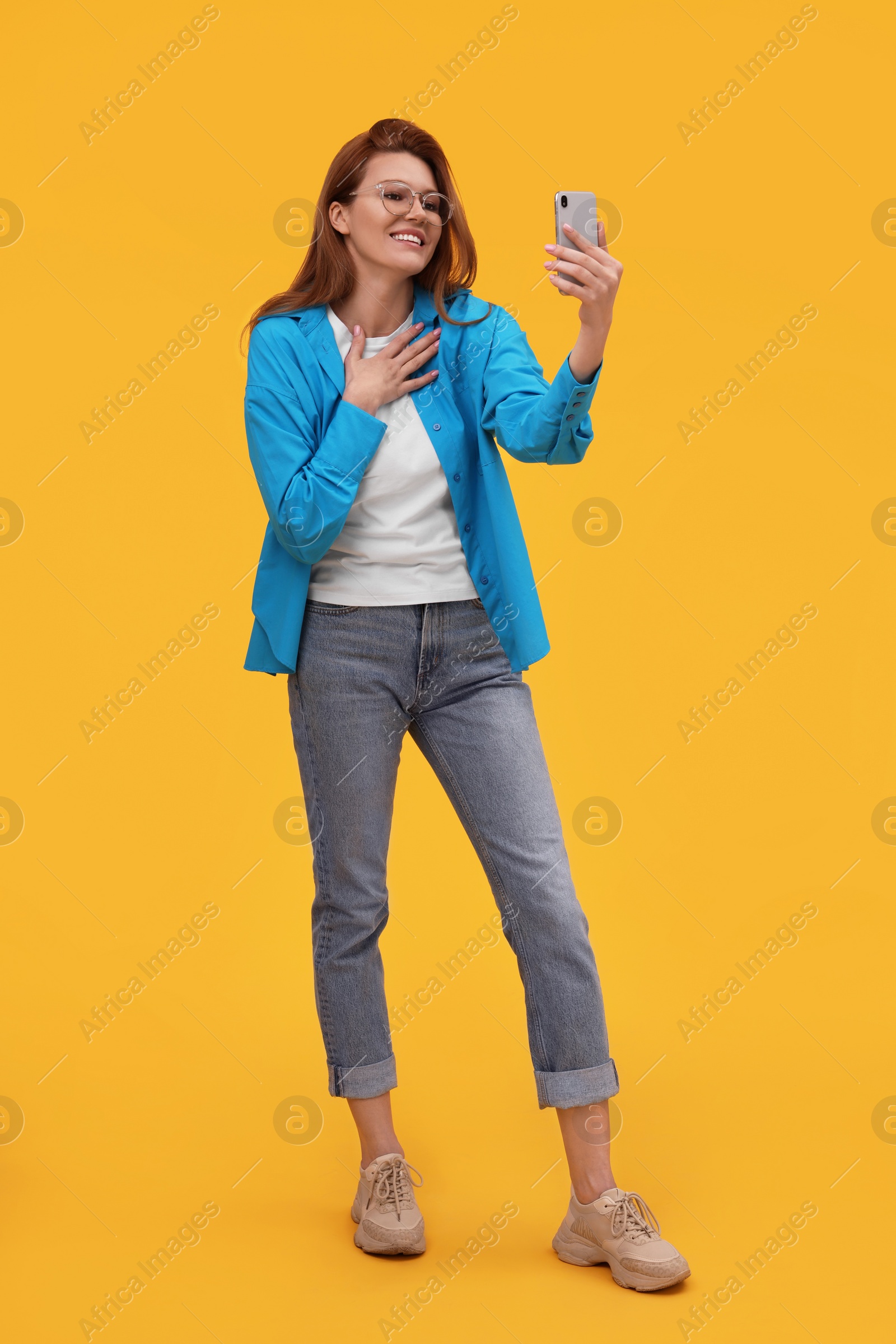 Photo of Beautiful woman in eyeglasses taking selfie on orange background