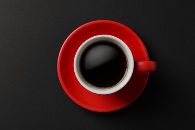 Cup with aromatic coffee on black background, top view