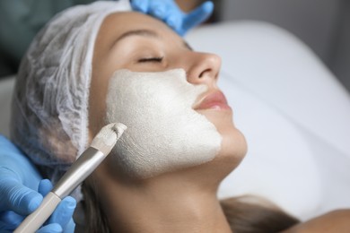 Cosmetologist applying mask on client's face in spa salon, closeup