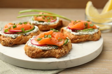 Tasty canapes with salmon, cucumber, radish and cream cheese on wooden table, closeup