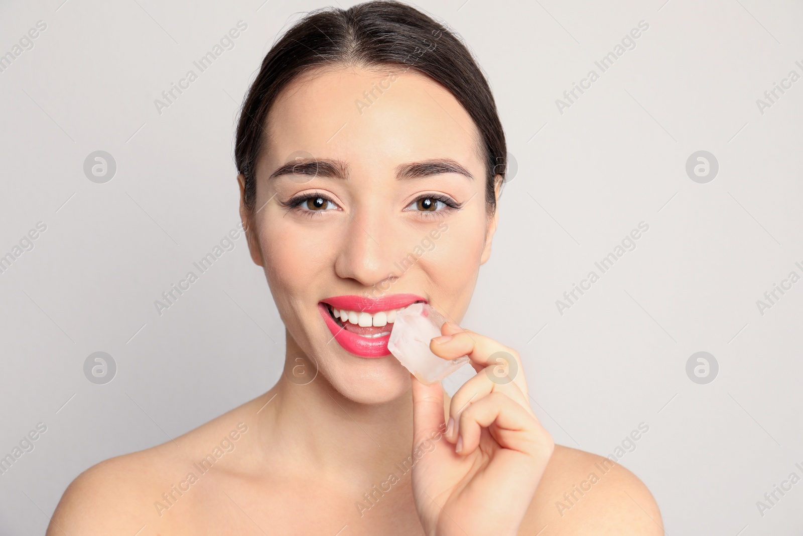 Photo of Young woman with ice cube on light background