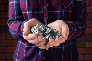 Photo of Woman with silver nuggets against brick background, closeup