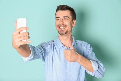 Young handsome man taking selfie against color background