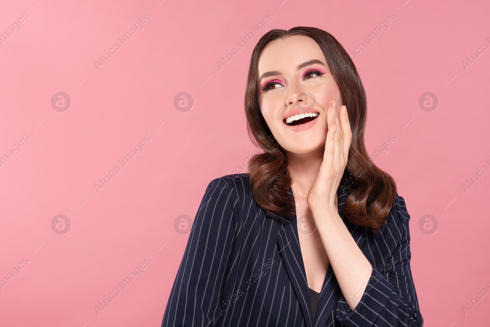 Photo of Portrait of beautiful young woman with makeup and gorgeous hair styling on pink background. Space for text