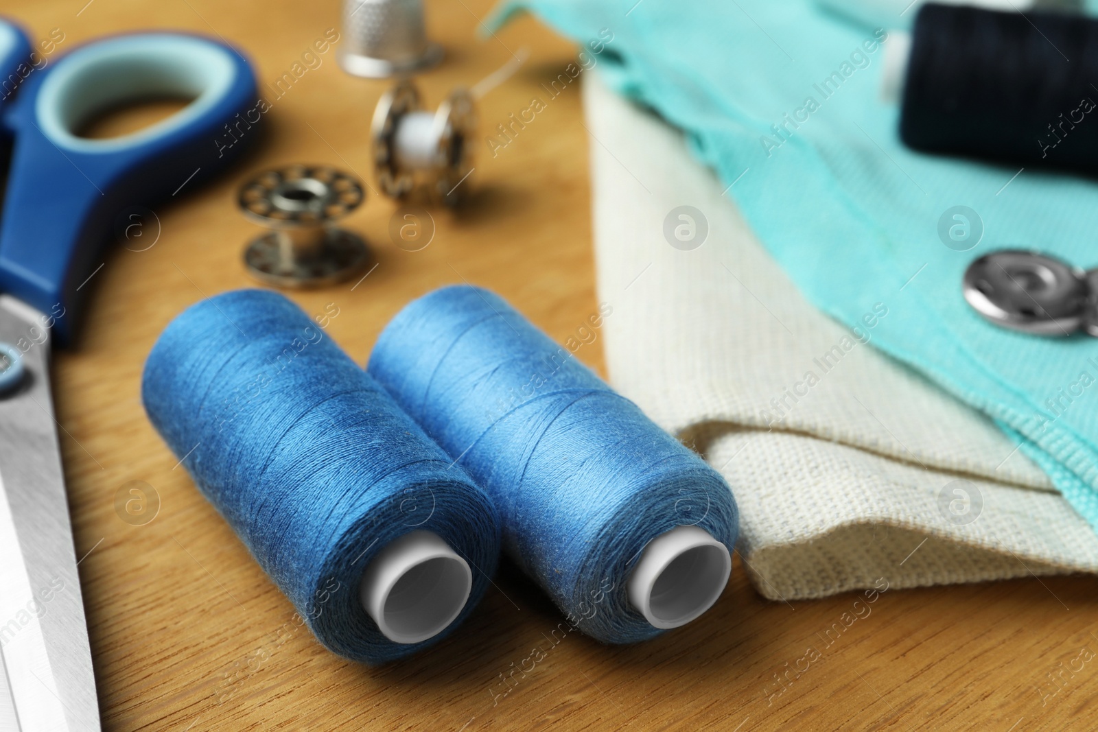 Photo of Spools of threads and sewing tools on wooden table, closeup