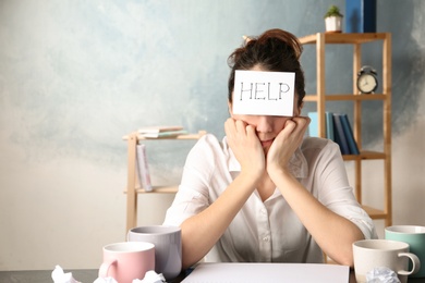 Photo of Young woman with note HELP on forehead at workplace. Space for text