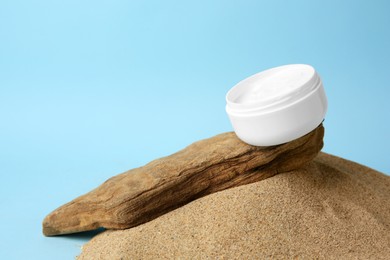 Jar of cream and bark on sand against light blue background, space for text. Cosmetic product