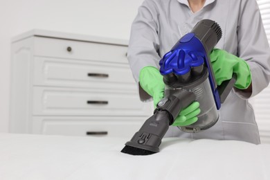 Photo of Woman in gloves disinfecting mattress with vacuum cleaner indoors, closeup. Space for text