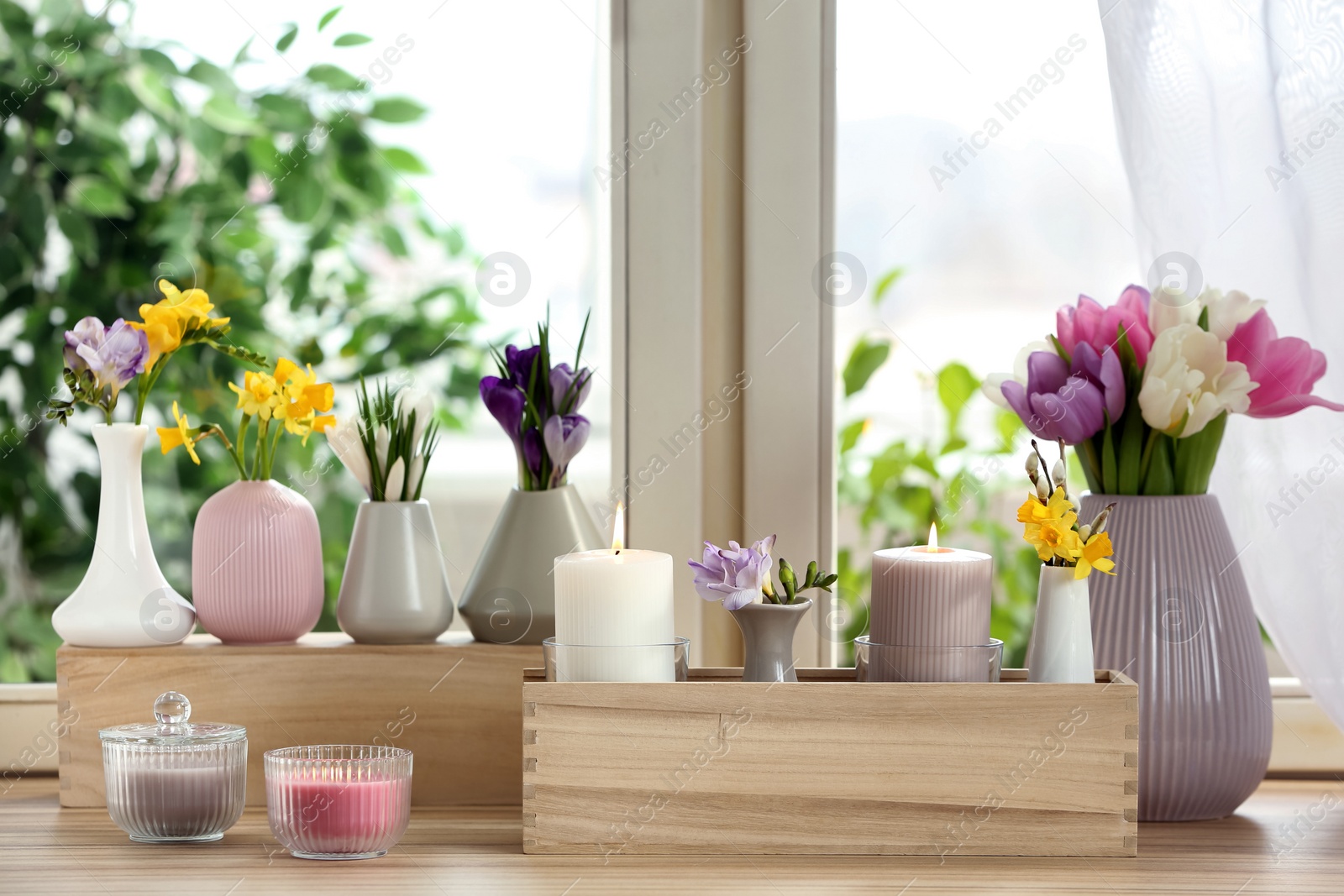 Photo of Beautiful spring flowers with burning candles on window sill