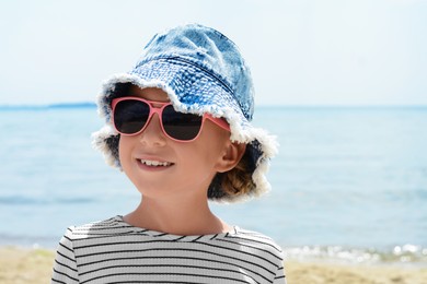 Little girl wearing sunglasses and hat at beach on sunny day. Space for text