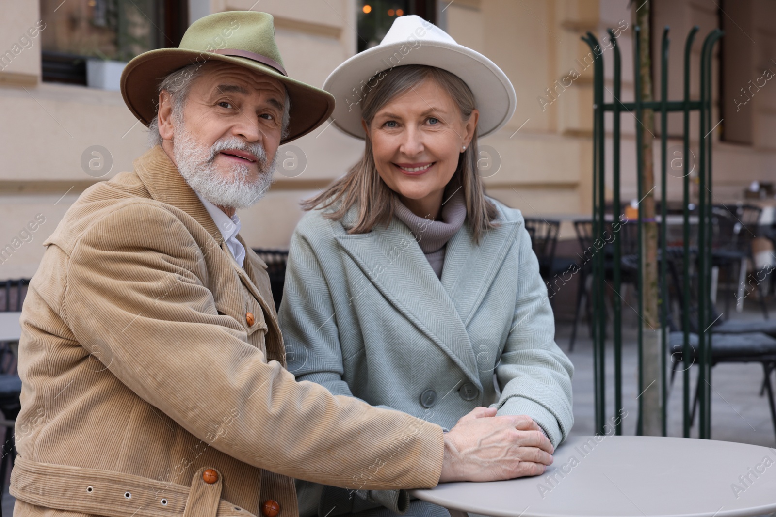 Photo of Portrait of affectionate senior couple sitting in outdoor cafe, space for text