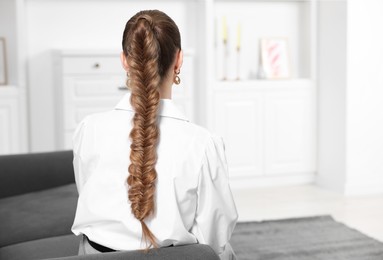 Photo of Woman with braided hair on sofa at home, back view. Space for text