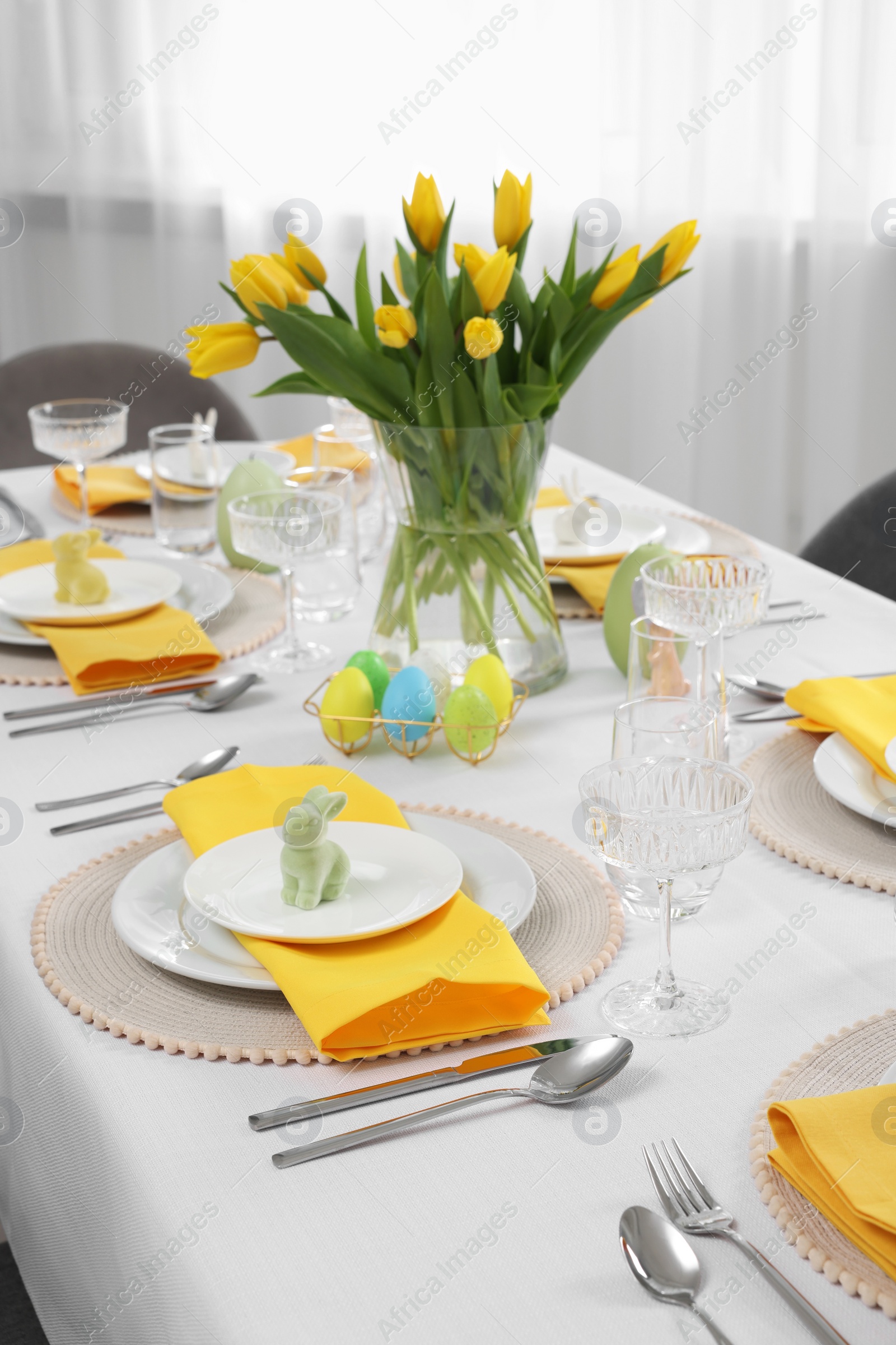 Photo of Festive table setting with glasses, painted eggs and vase of tulips. Easter celebration