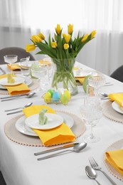 Festive table setting with glasses, painted eggs and vase of tulips. Easter celebration