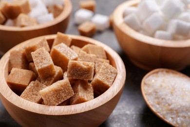 Bowls and spoon with different types of sugar on table, closeup