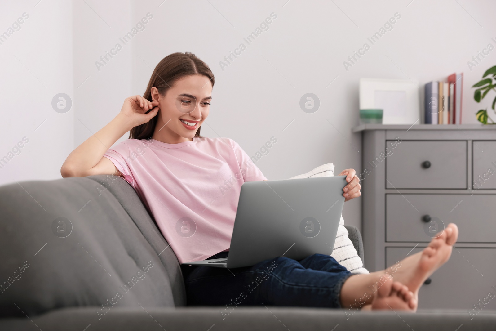 Photo of Happy young woman with laptop on sofa at home