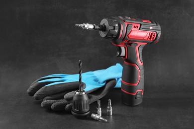 Electric screwdriver, drill chuck, bits and gloves on dark grey background