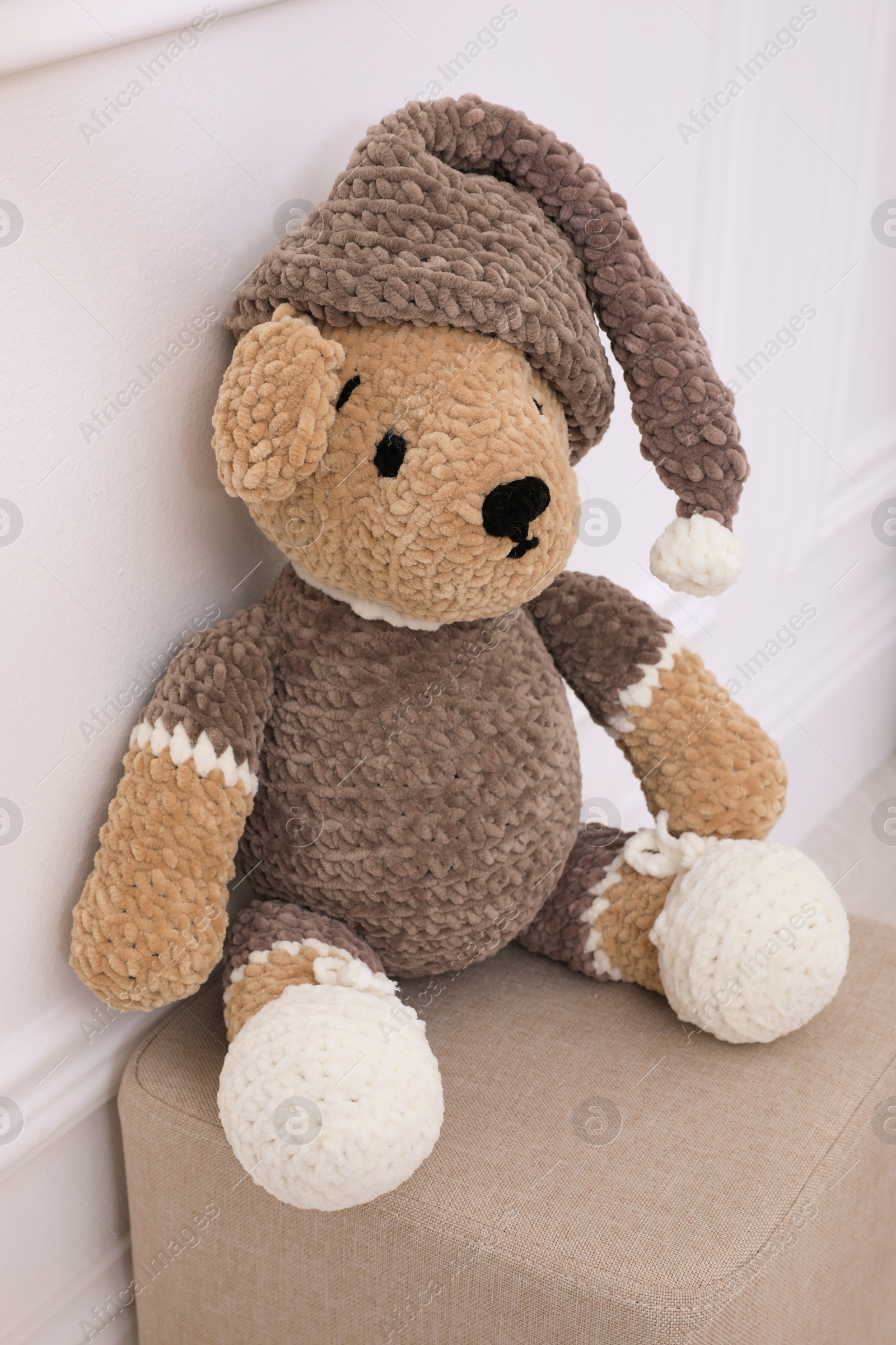 Photo of Adorable brown toy bear on pouf near white wall