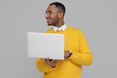 Photo of Happy young intern working on laptop against light grey background