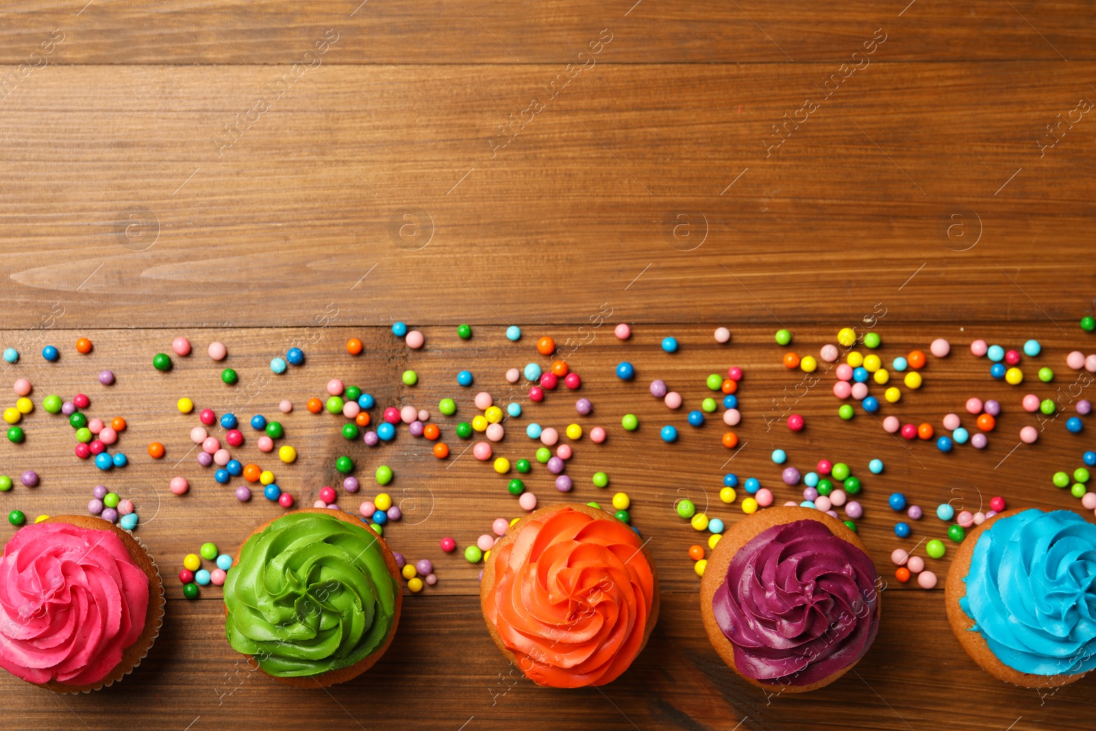 Photo of Flat lay composition with delicious colorful cupcakes on wooden table. Space for text
